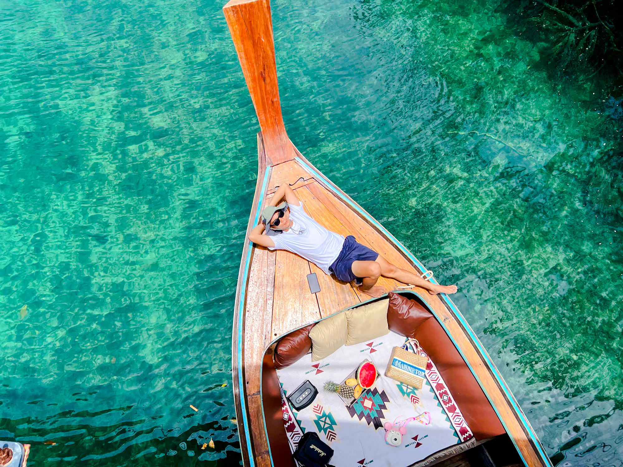 Longtail boat on clear waters near Phi Phi, person relaxing on deck with lunch setup.
