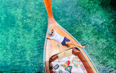 Longtail boat on clear waters near Phi Phi, person relaxing on deck with lunch setup.