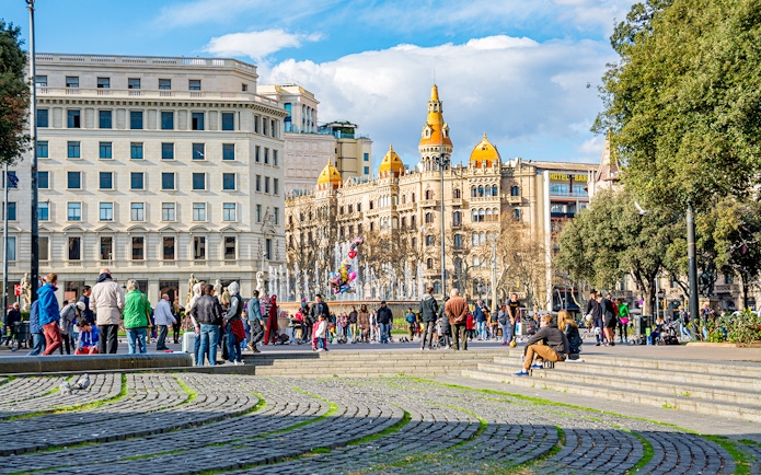 Aerobus driving through Placa de Catalunya, central square in Barcelona, Spain, with people and historic buildings.