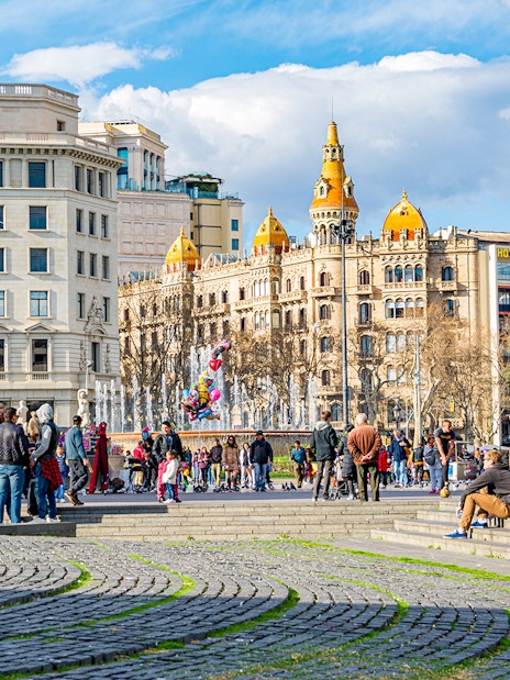 Aerobus driving through Placa de Catalunya, central square in Barcelona, Spain, with people and historic buildings.