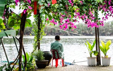 Man sitting by a river under flowering vines in Hoi An countryside.