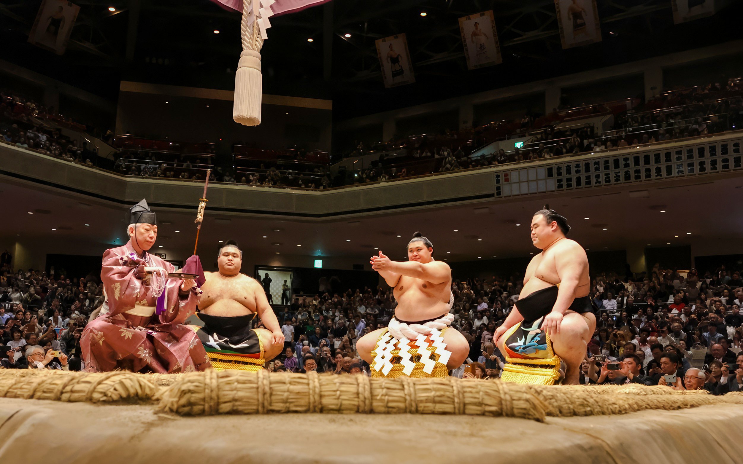 Sumo wrestlers in traditional attire seated in a crowded arena.