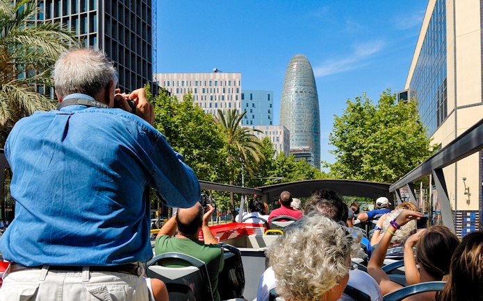 Tourists on Barcelona hop-on hop-off bus viewing Torre Glòries.