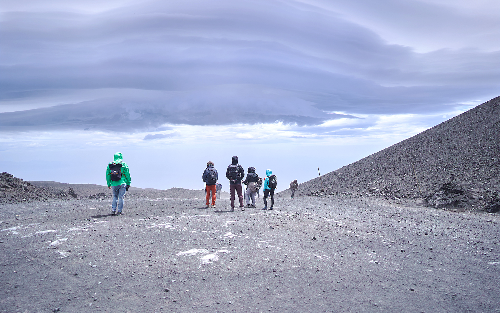 Skiers descending snowy slopes of Mount Etna, Sicily, with volcanic landscape in the background.