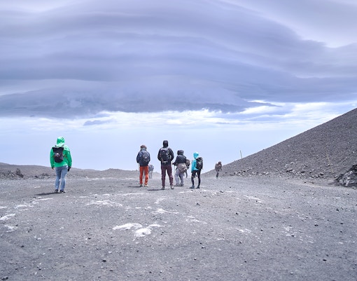 Skiers descending snowy slopes of Mount Etna, Sicily, with volcanic landscape in the background.