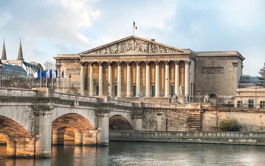 French National Assembly building in Paris with bridge over the Seine River.