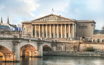 French National Assembly building in Paris with bridge over the Seine River.