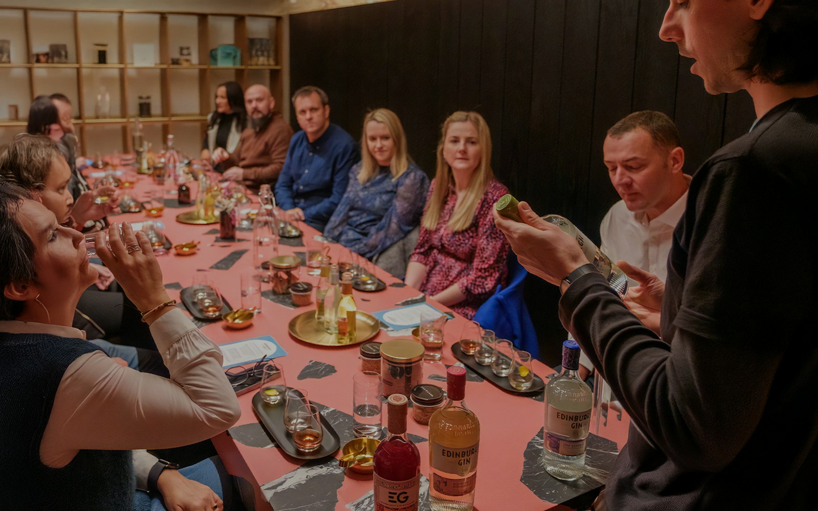 Tour group tasting gin at Edinburgh distillery, guide explaining bottle details.