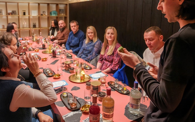 Tour group tasting gin at Edinburgh distillery, guide explaining bottle details.