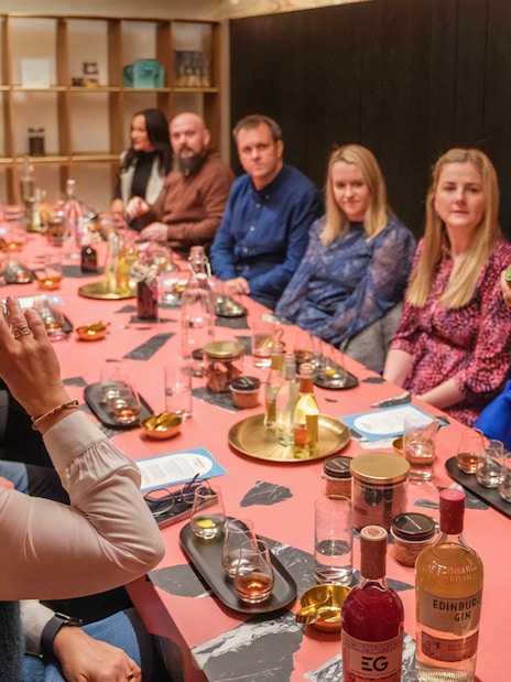 Tour group tasting gin at Edinburgh distillery, guide explaining bottle details.