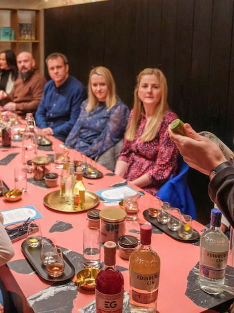 Tour group tasting gin at Edinburgh distillery, guide explaining bottle details.