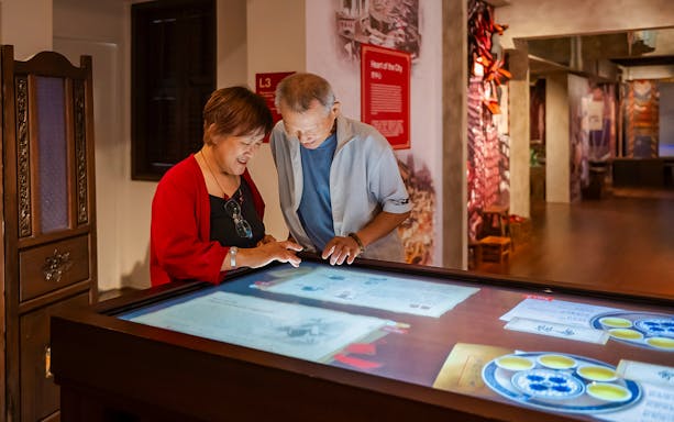 Visitors interacting with a digital exhibit at Chinatown Heritage Centre's Arrival and Settling In display.