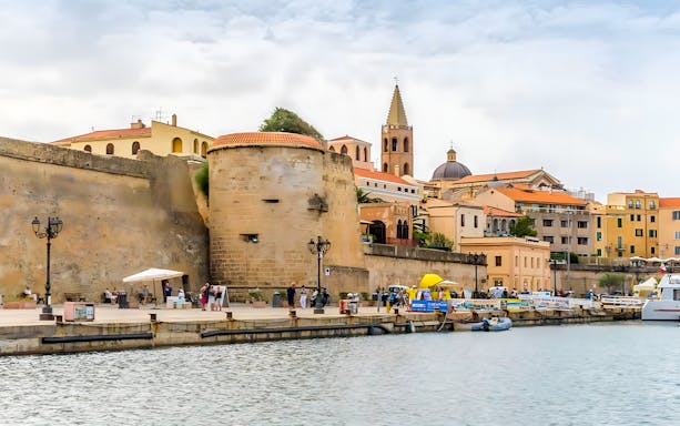 Alghero waterfront with historic walls and bell tower in the background.