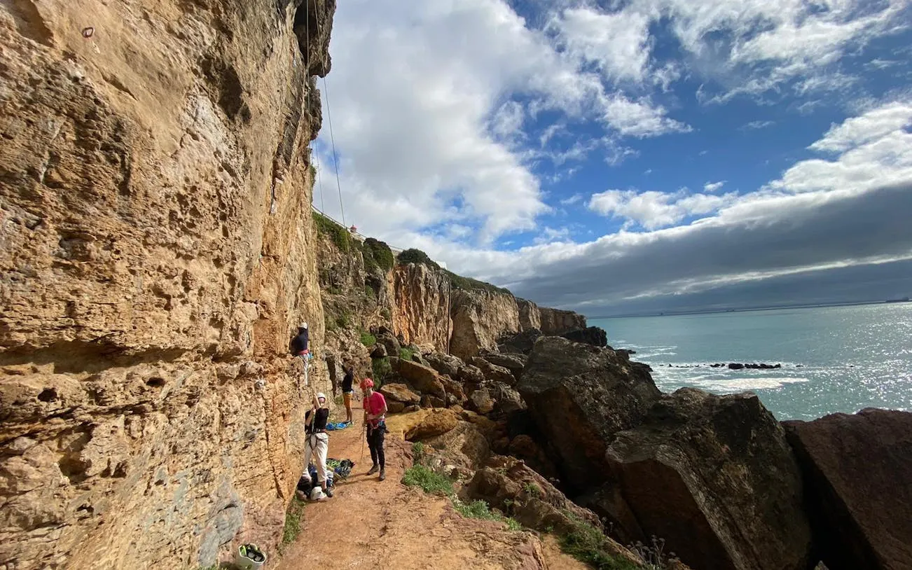 Rock climbers scaling cliffs on Guia Cascais tour with ocean view.