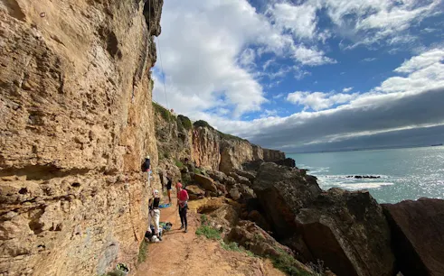 Rock climbers scaling cliffs on Guia Cascais tour with ocean view.