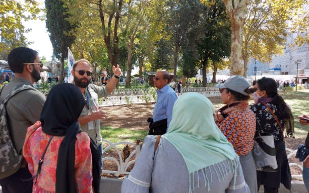 Tour group with guide in Istanbul park, discussing attractions with E-pass benefits.