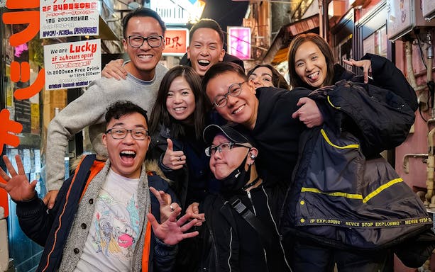Tourists smiling and posing in a lively alley during the Shinjuku Local Bar & Izakaya Crawl in Tokyo.