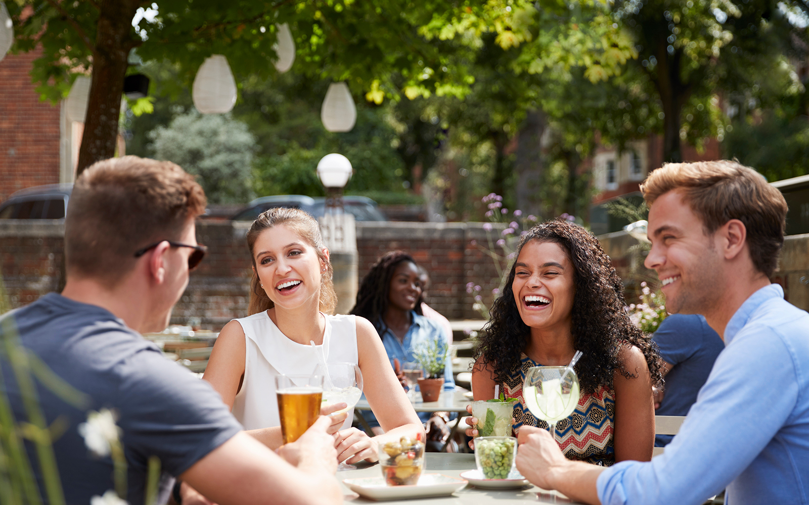 Friends Sitting At Table In Pub Garden Enjoying Drinks Together