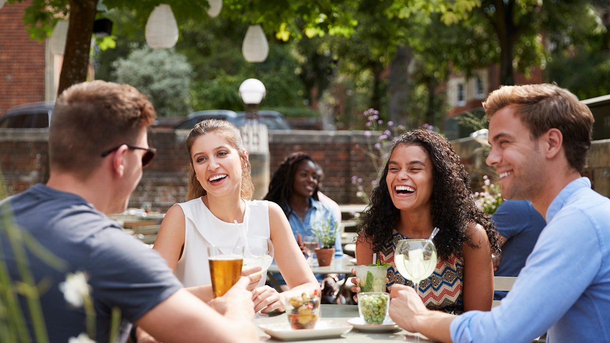 Group enjoying drinks at an outdoor café in a garden setting.