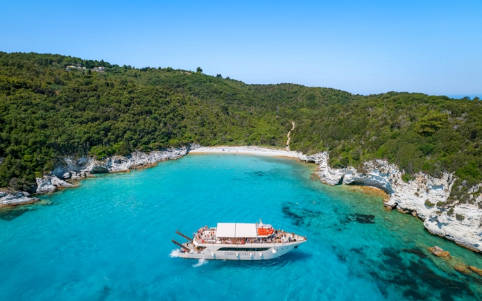 Boat approaching Voutoumi Beach, Antipaxos, with turquoise waters and lush greenery.