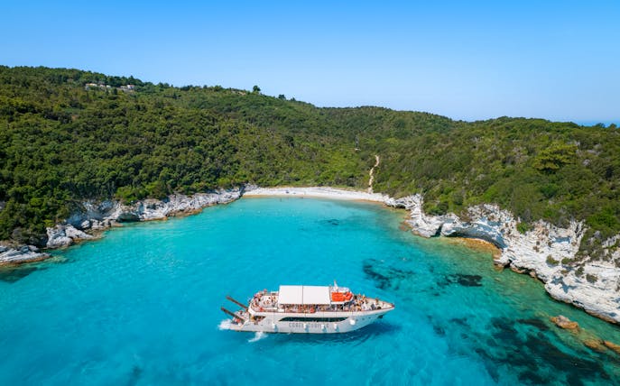 Boat approaching Voutoumi Beach, Antipaxos, with turquoise waters and lush greenery.