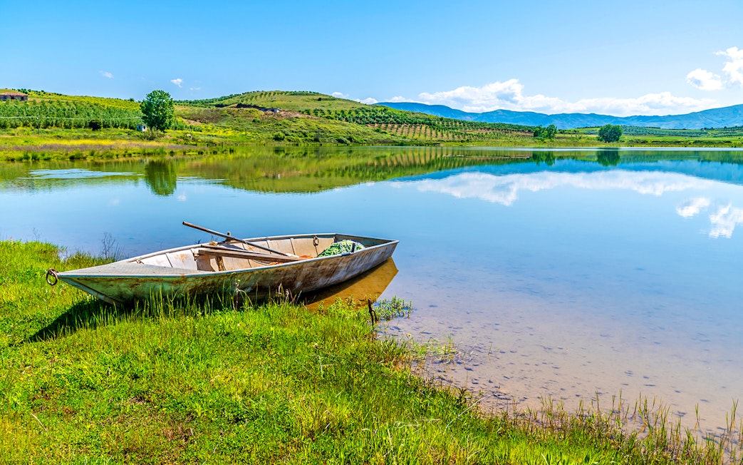 Boat on the shore of Belshi Lake with hills in the background.