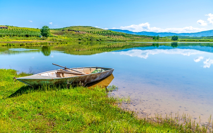 Boat on the shore of Belshi Lake with hills in the background.