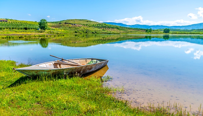 Boat on the shore of Belshi Lake with hills in the background.