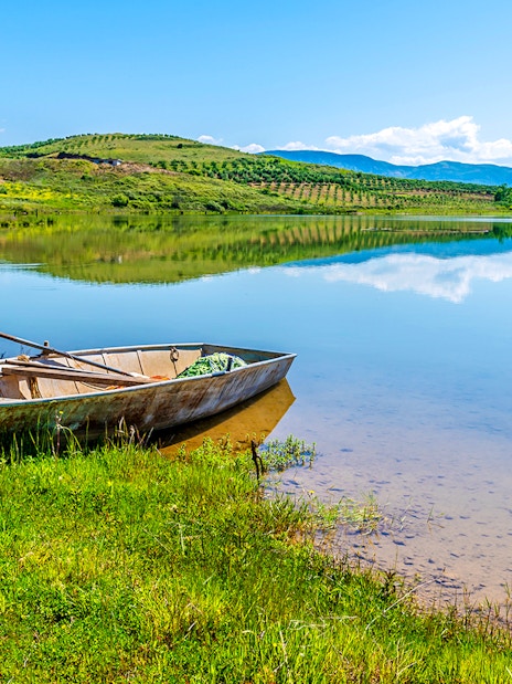 Boat on the shore of Belshi Lake with hills in the background.