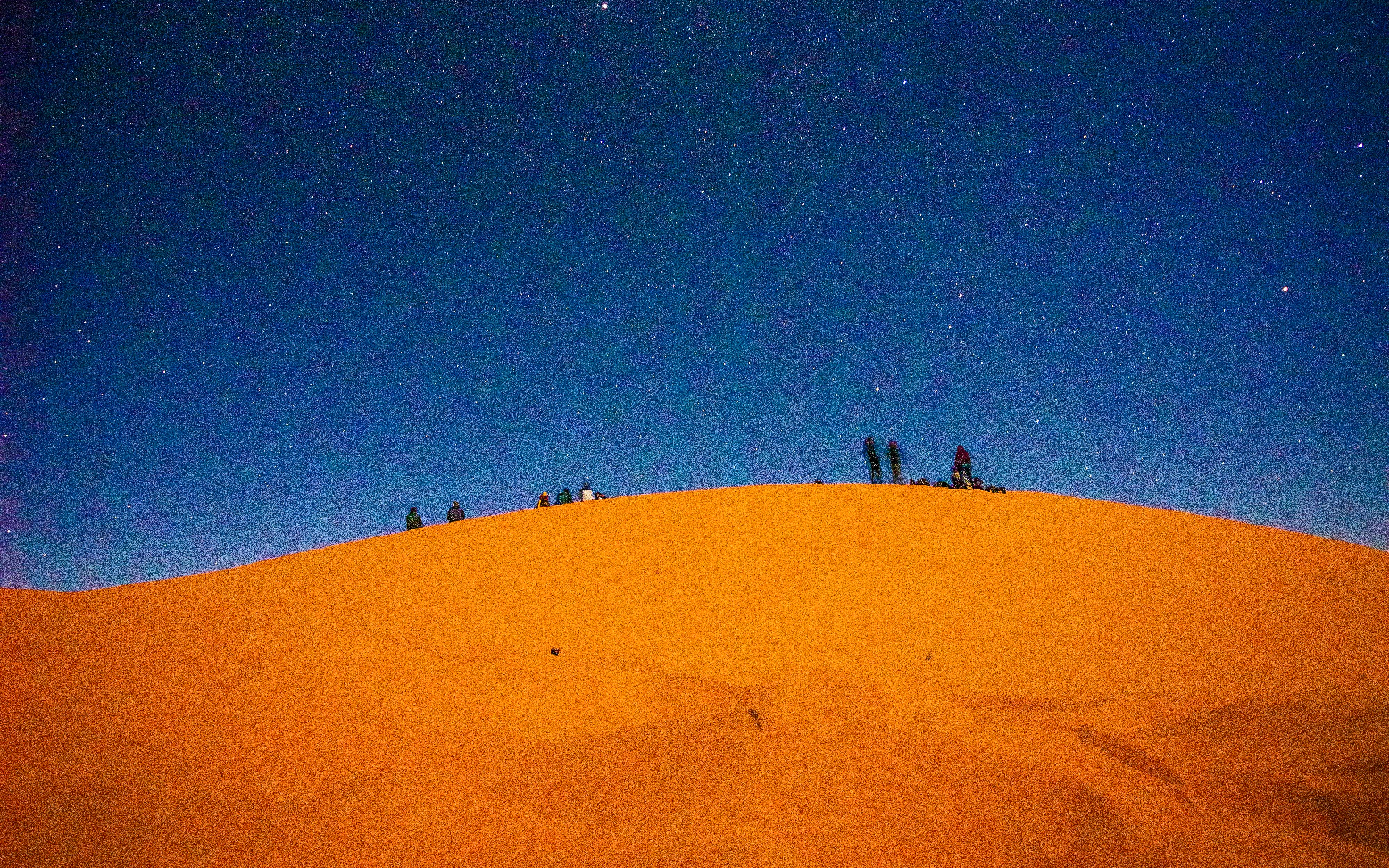 Camel riders silhouetted on a dune under a starry sky, Doha desert safari.