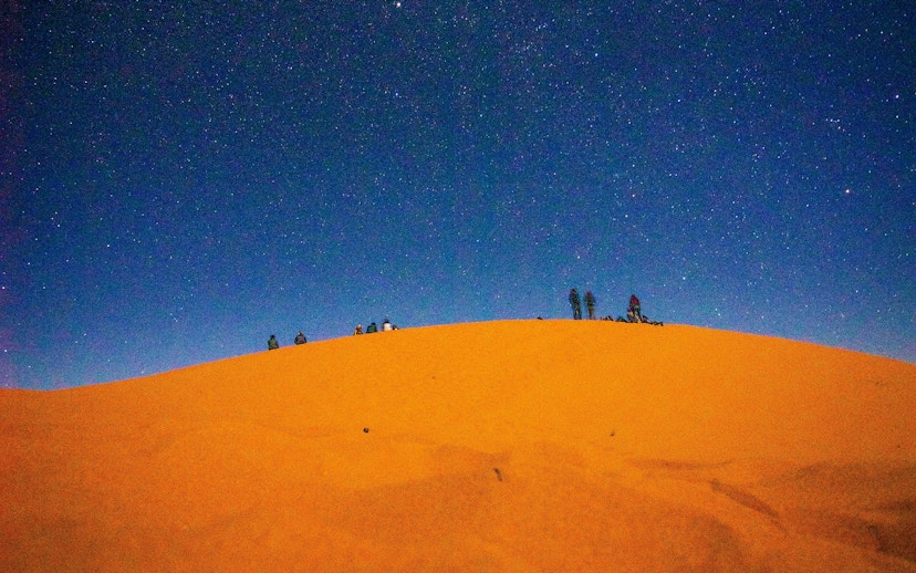 Camel riders silhouetted on a dune under a starry sky, Doha desert safari.