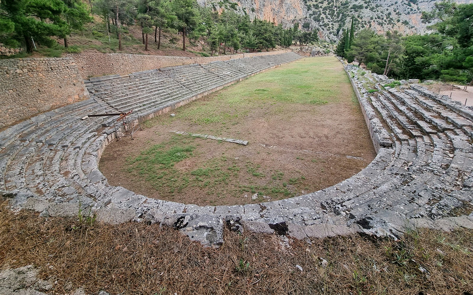 Ancient stadium at Delphi Archaeological Site with stone seating and grassy field.