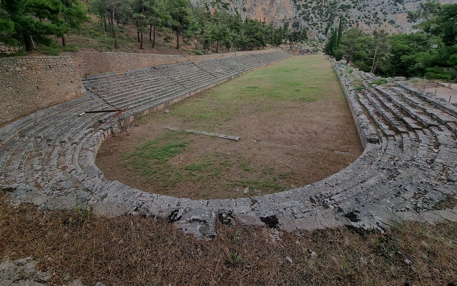 Ancient stadium at Delphi Archaeological Site with stone seating and grassy field.