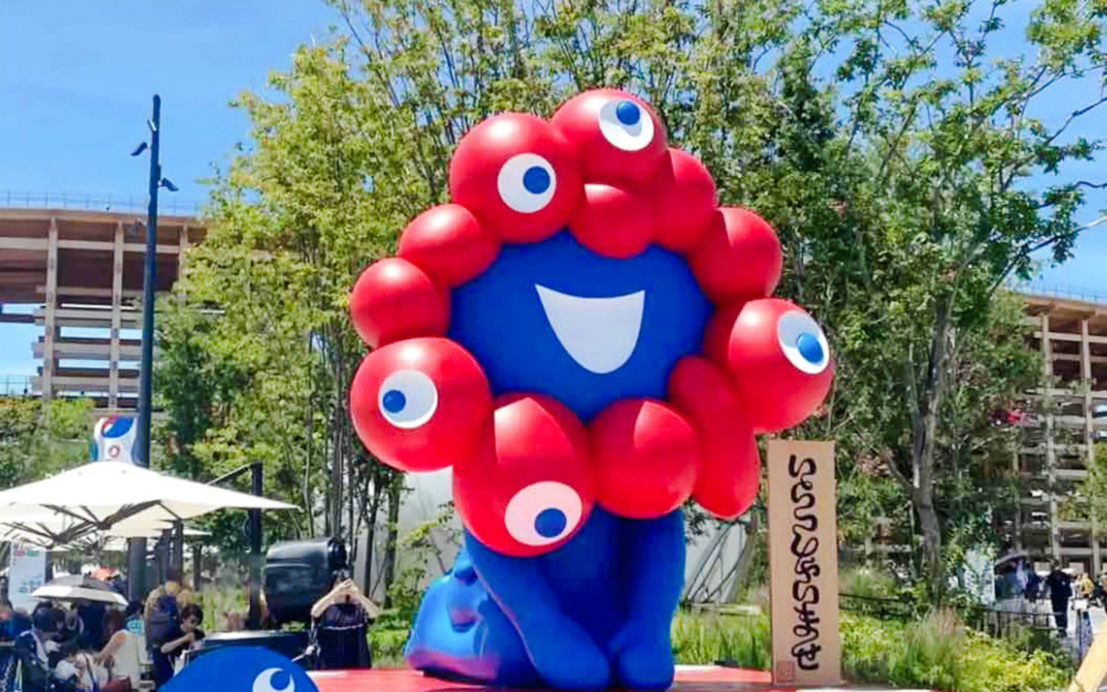 Osaka Expo mascot with red and blue design in outdoor setting.