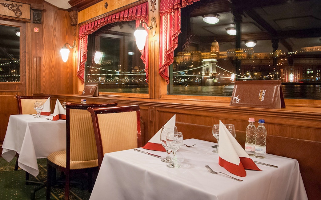 Interior dining area of New Year’s Eve Cruise in Budapest with view of illuminated cityscape.