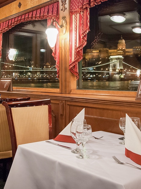 Interior dining area of New Year’s Eve Cruise in Budapest with view of illuminated cityscape.