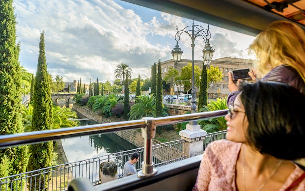 Tourists seated inside Palma de Mallorca Hop-On Hop-Off Bus, viewing city landmarks through large windows.