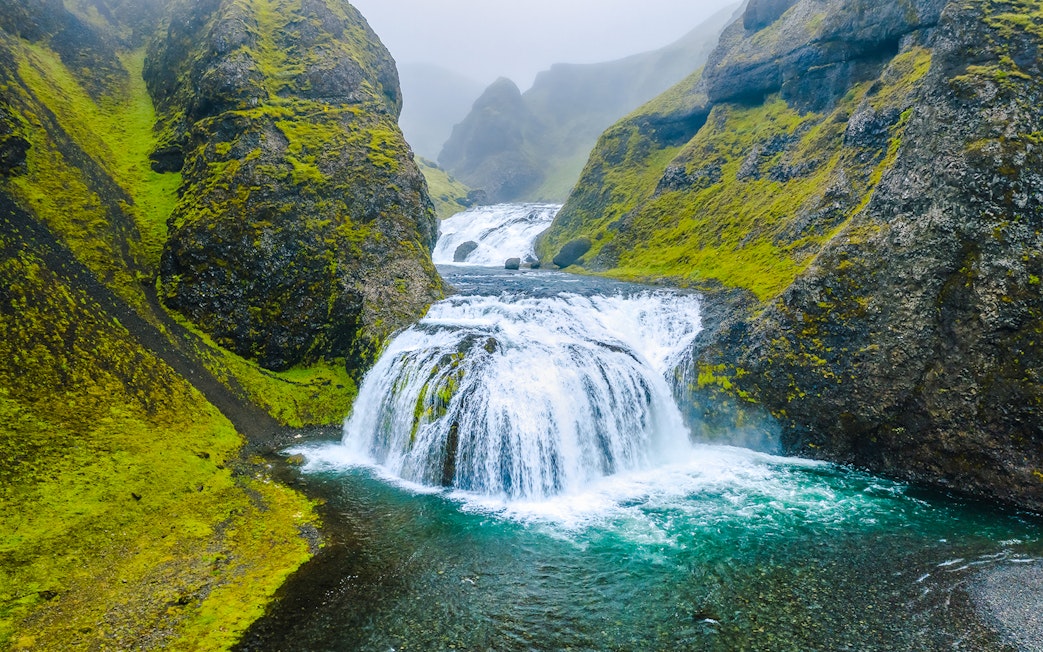 Stjornarfoss waterfall cascading between moss-covered cliffs in Southern Iceland.