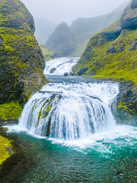 Stjornarfoss waterfall cascading between moss-covered cliffs in Southern Iceland.