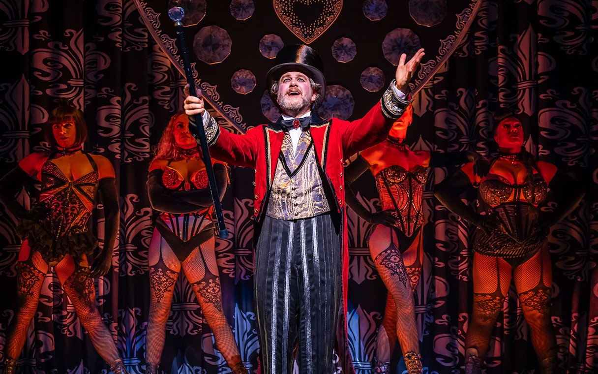 Performer in red coat with dancers at Moulin Rouge! The Musical stage show.