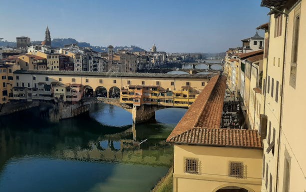Ponte Vecchio over the Arno River in Florence, Italy, with historic buildings lining the riverbank.