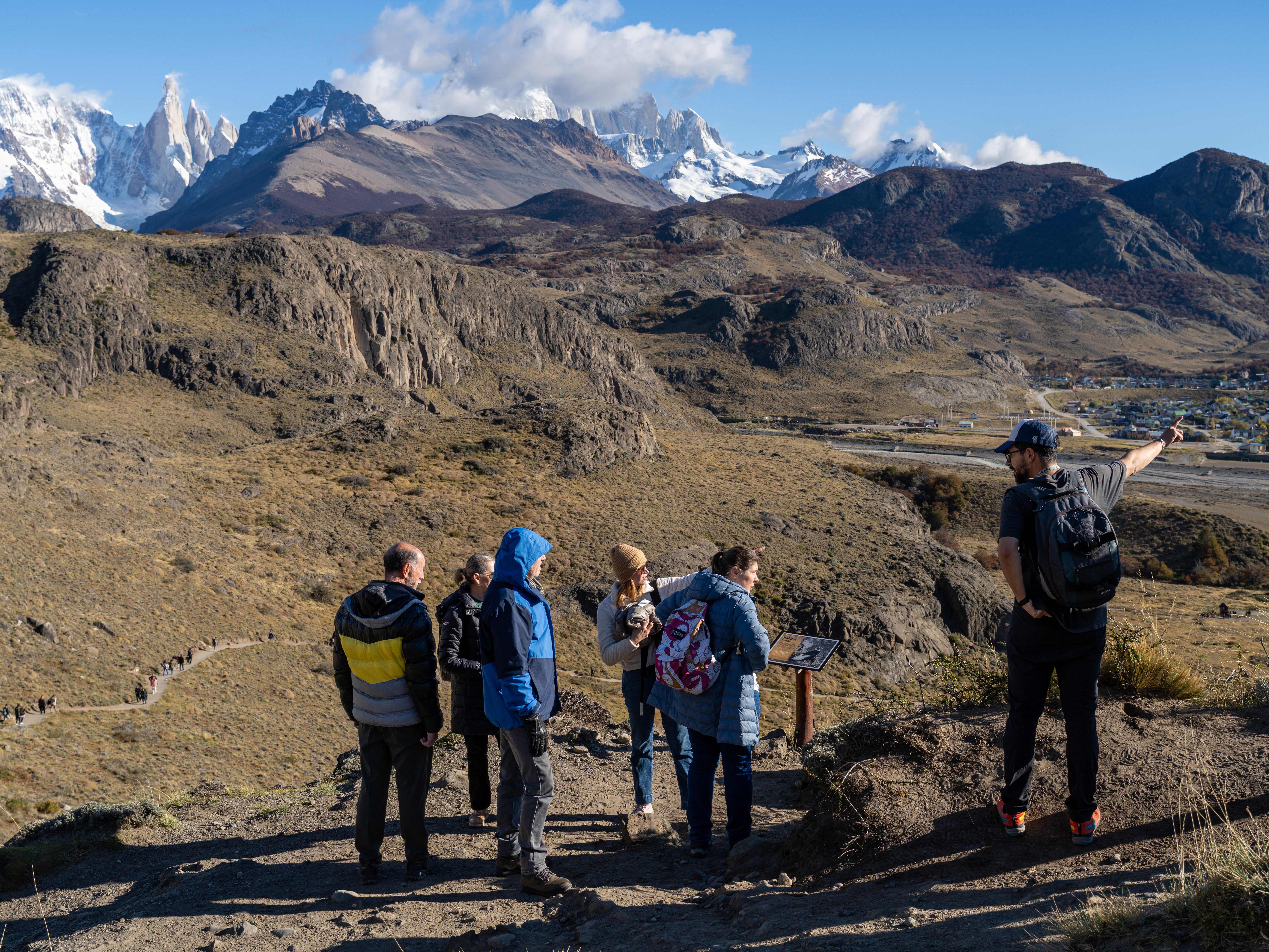 Tourists on a hiking trail in El Chaltén, Argentina, with a guide pointing towards the mountains.
