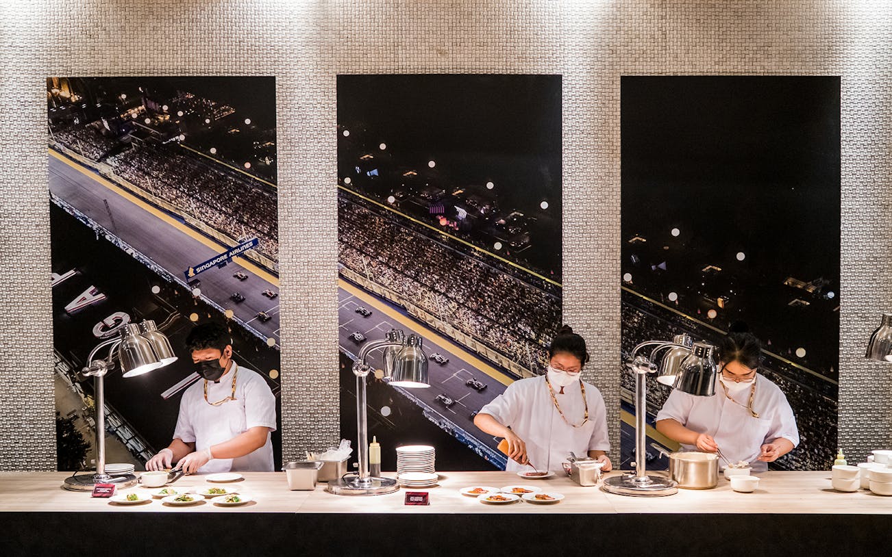 Chefs preparing dishes in front of Singapore Grand Prix track backdrop, Formula 1 Hospitality Package.