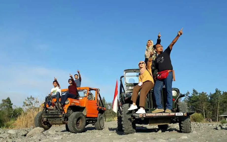 Jeep tour group pointing at sunrise on Merapi, Indonesia, with two jeeps on rocky terrain.