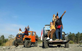 Jeep tour group pointing at sunrise on Merapi, Indonesia, with two jeeps on rocky terrain.
