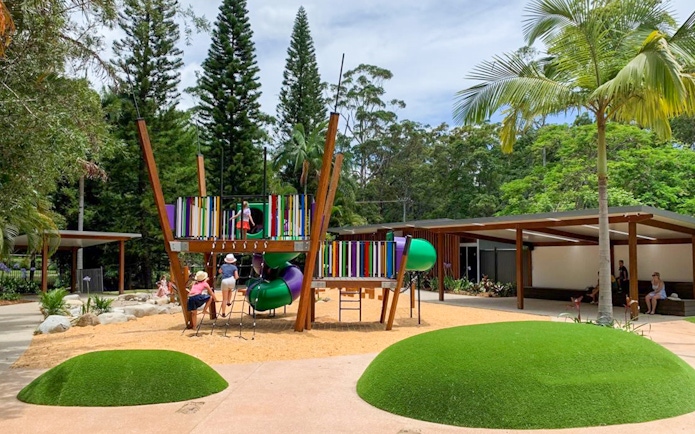 Children playing on colorful playground equipment at Amaze World, surrounded by trees and greenery.