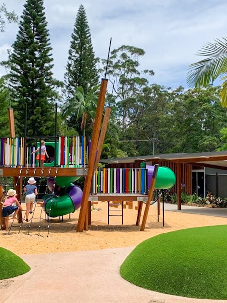 Children playing on colorful playground equipment at Amaze World, surrounded by trees and greenery.