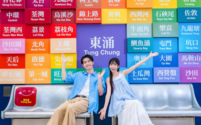 Couple sitting in front of colorful Tung Chung sign, preparing for Ngong Ping 360 cable car on Lantau Island.