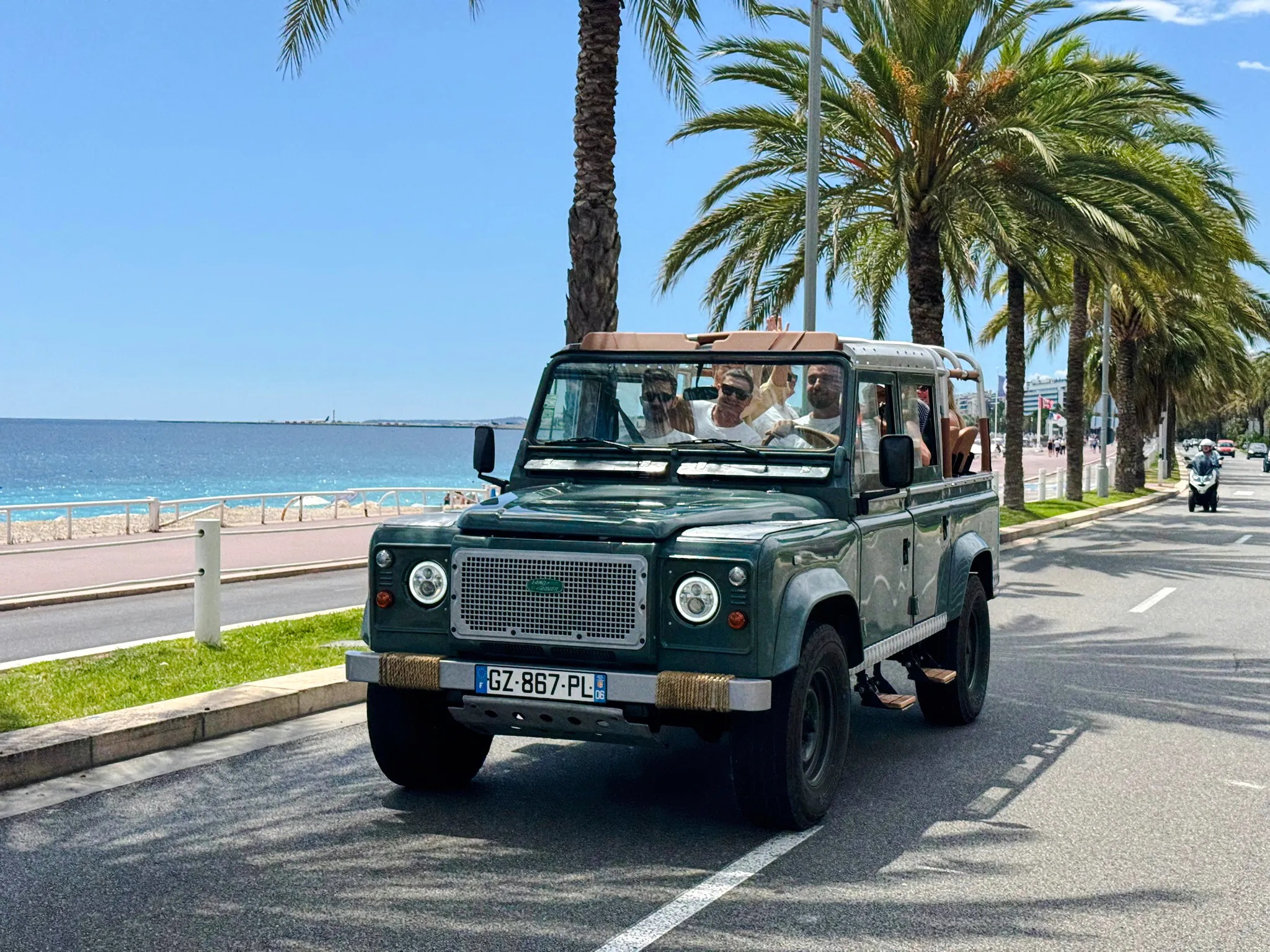 Land Rover driving along Nice's coastal road with palm trees and sea view.
