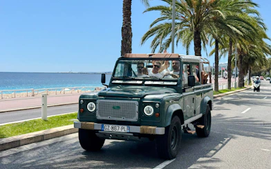 Land Rover driving along Nice's coastal road with palm trees and sea view.